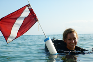 Dr. Sadler in the water in scuba gear holding a white and red flag