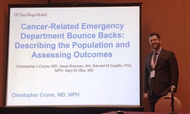 Dr. Coyne standing in front of a projected display of a cancer related emergency department bounce backs presentation